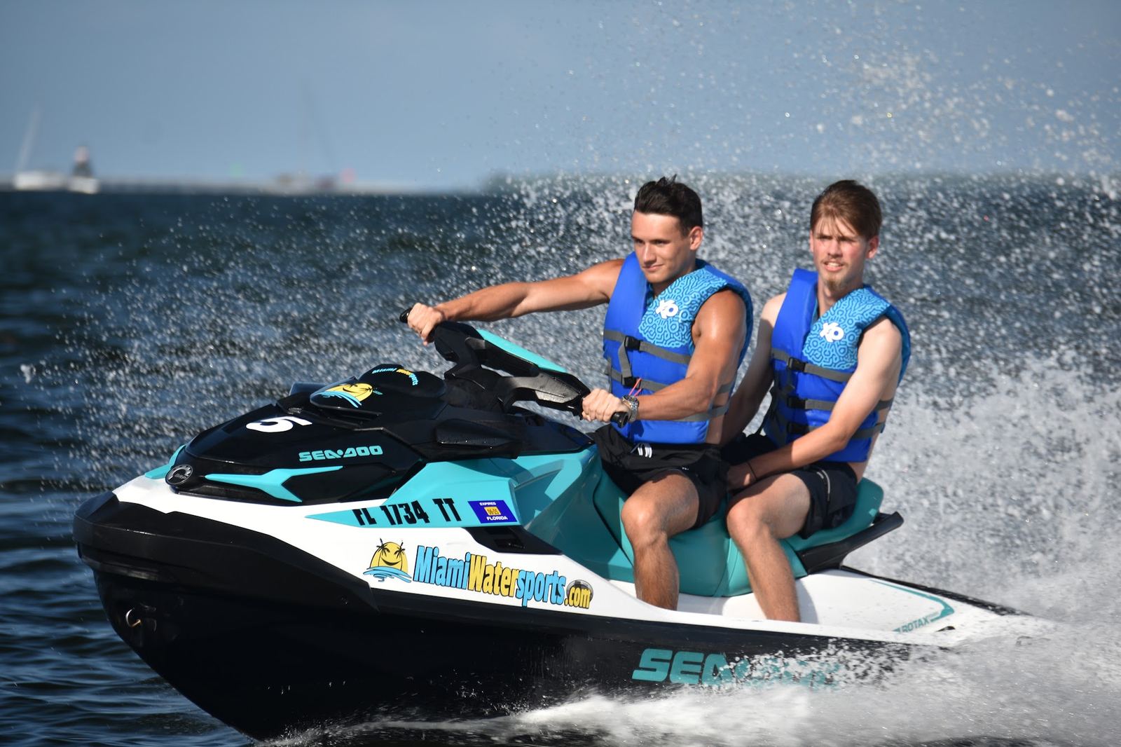 Two riders on a jet ski heading toward the camera on the bay